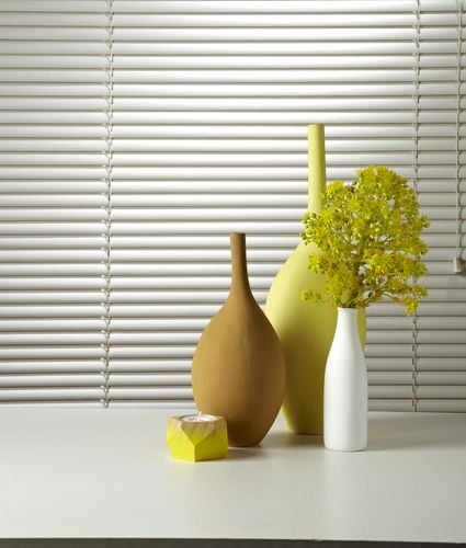Close up of vases and a candle in front of a window with white venetian blinds