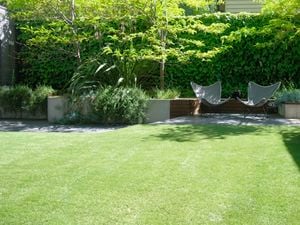 A large backyard with a smooth green lawn of Tuff Turf artificial grass and paved seating area plus raised garden beds.
