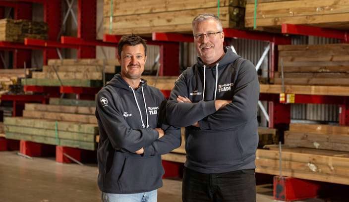 Two males wearing green Movember trade hoodies in a Bunnings Timberyard.