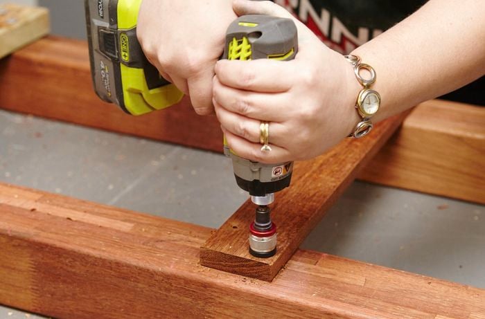 Person drilling spacer to wooden table legs.