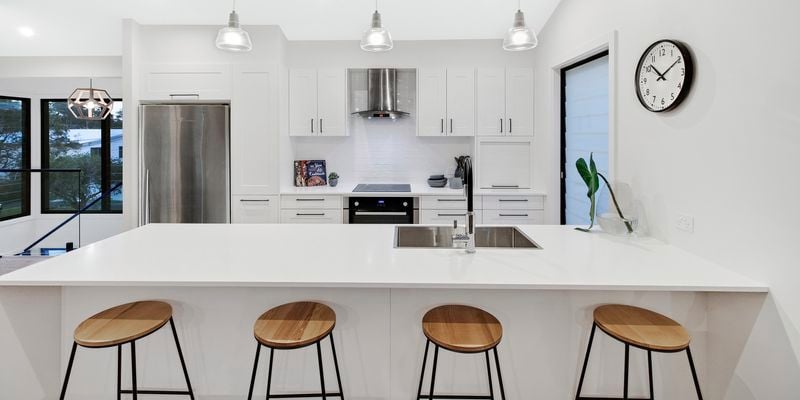 Shot of white kitchen with black accents and four stools in-front of benchtop.