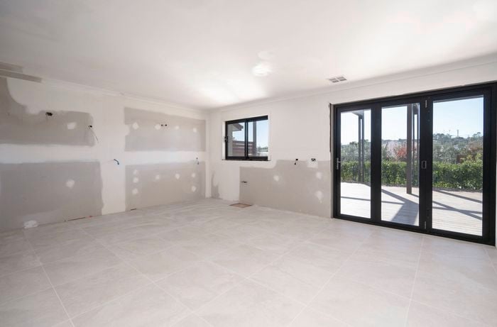 A newly constructed kitchen space features tiled floors, unfinished walls with plumbing and electrical points, a window, and large sliding glass doors opening to a garden view.