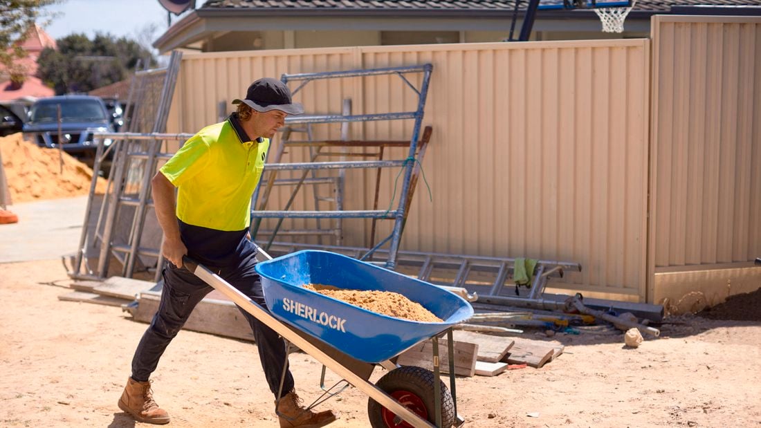 tradie wheeling a wheelbarrow on work site
