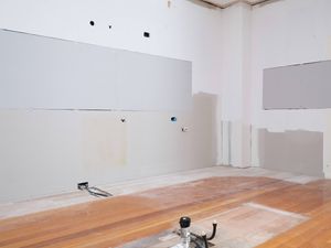 The image shows a completely stripped kitchen space with drywall patches and exposed flooring.