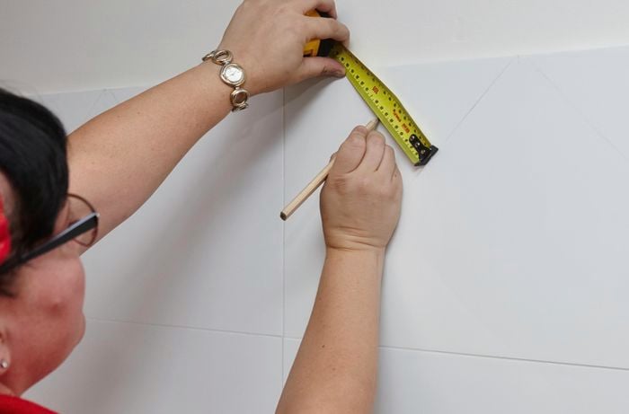 A person marking lines on splashback tiles in a kitchen