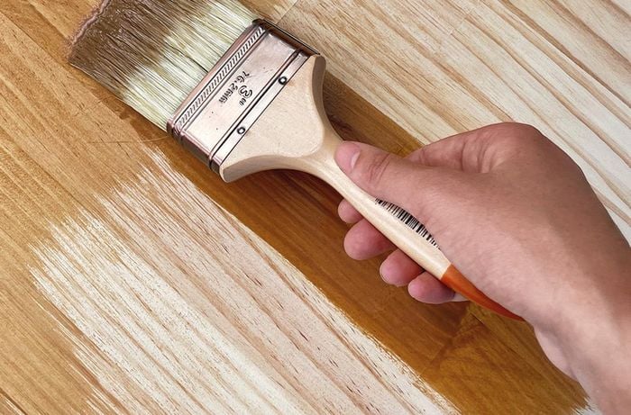 A person uses a paintbrush to apply a coat of varnish on a pine panel