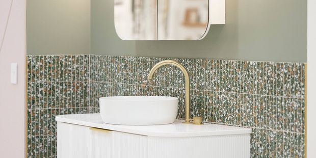 Floating vanity with vessel basin, gold tapware and mirrored cabinet against green tiled walls.