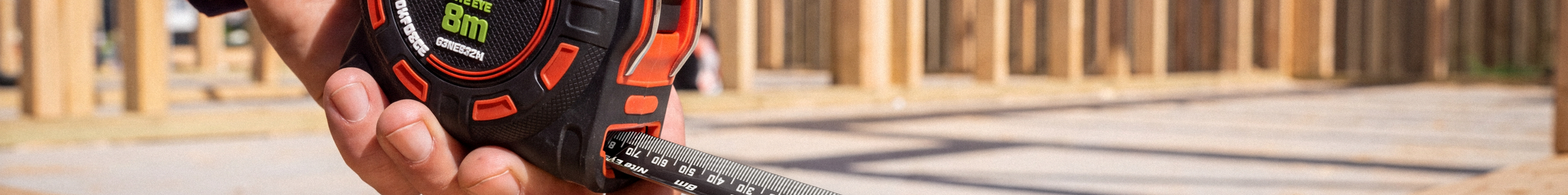 Close-up of a Crescent Lufkin Nite Eye tape measure extended across a timber beam while a worker marks measurements with a pencil.