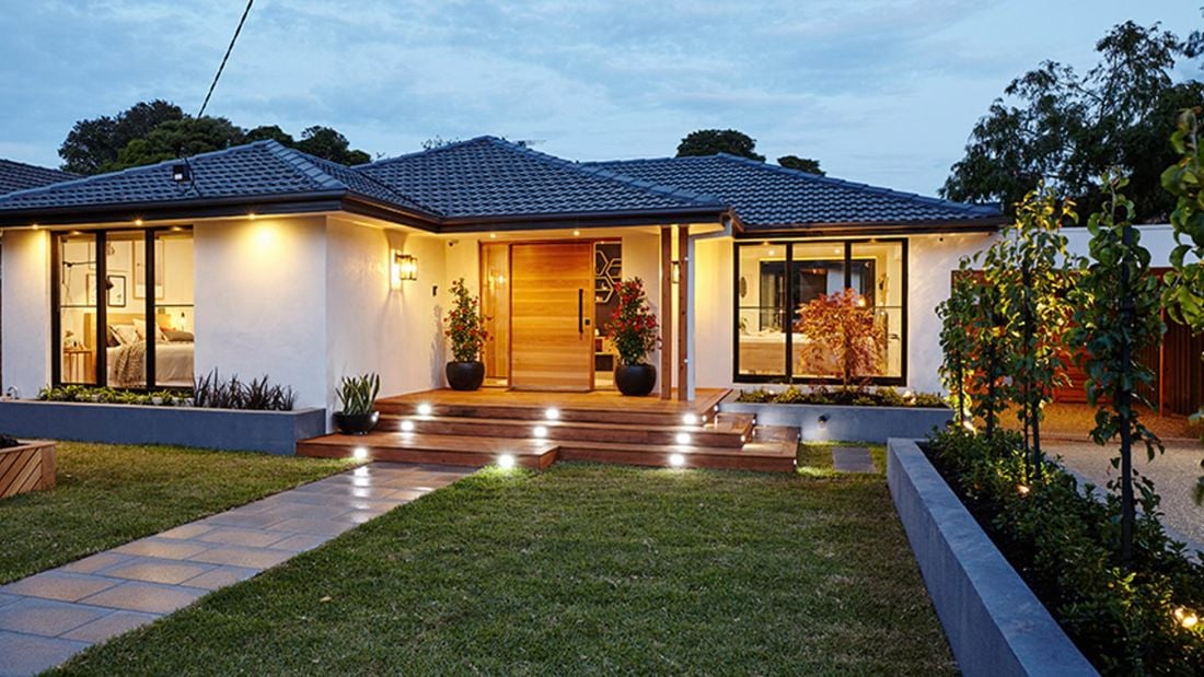 Outside of a lit up home in the evening, with path, decking and garden area.