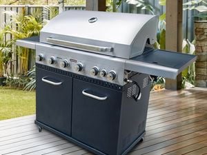 A large barbecue on a wooden deck in a backyard fenced off with glass