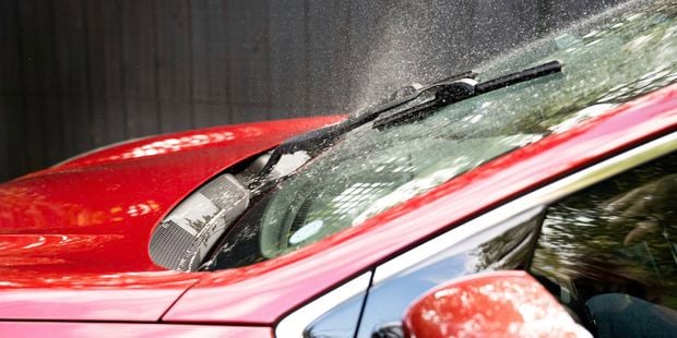 A red car’s windshield is sprayed with windscreen washer fluid.