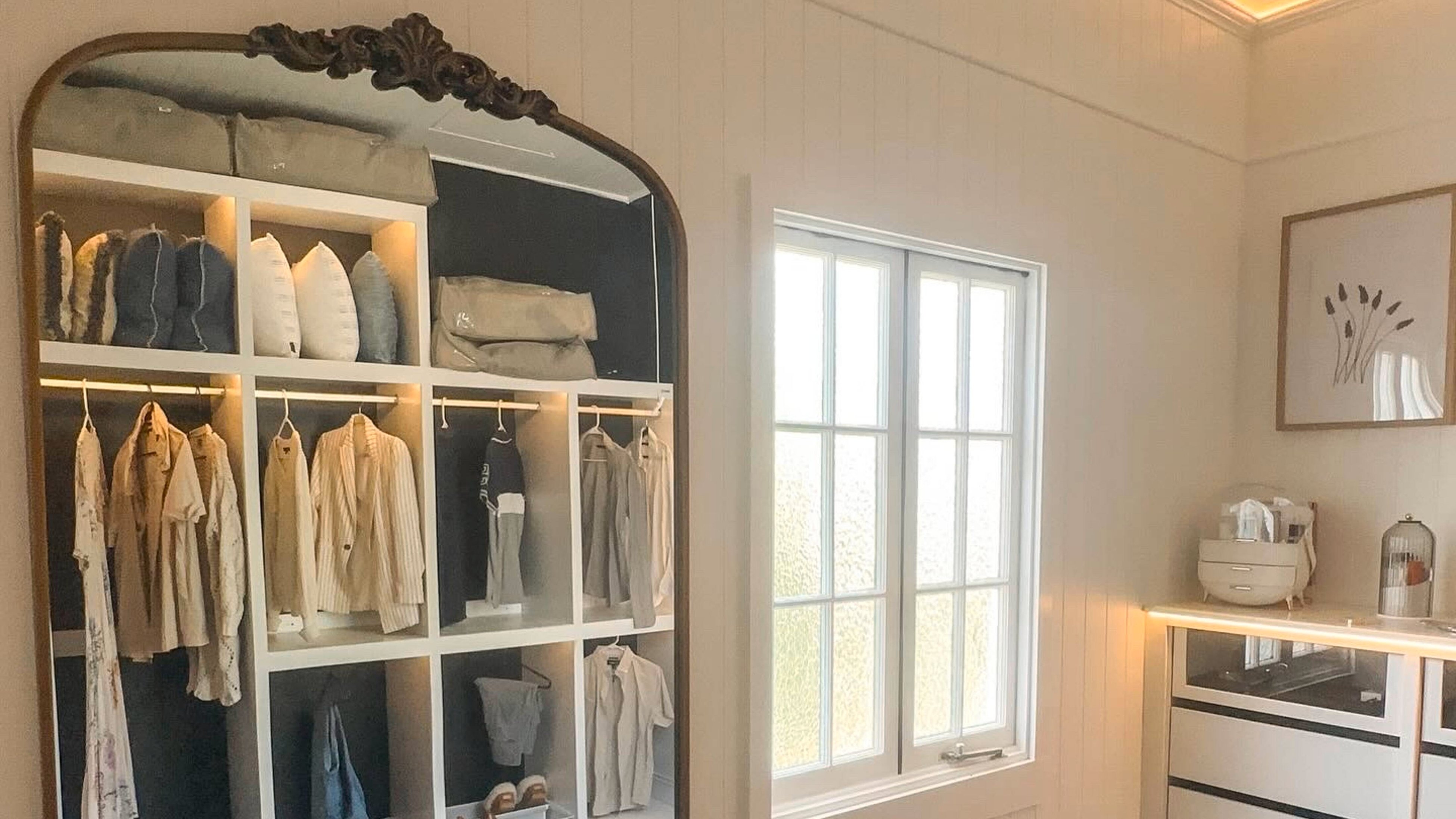 Tall standing mirror against wall in a bedroom across from the wardrobe seen in the reflection
