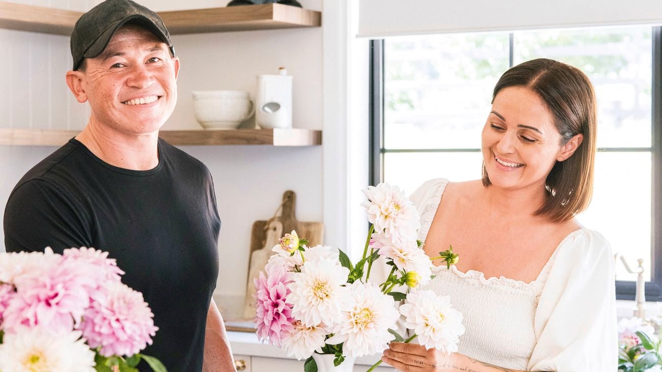 Katie and Rob of Little Lyndoch Flower Farm in a light kitchen, with pink and white flowers in a vase on a white countertop with fruit.
