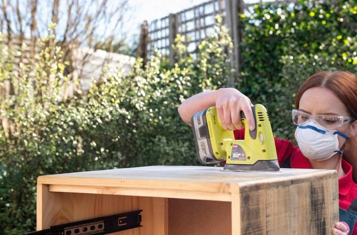 Person sanding a bedside table with a cordless sander