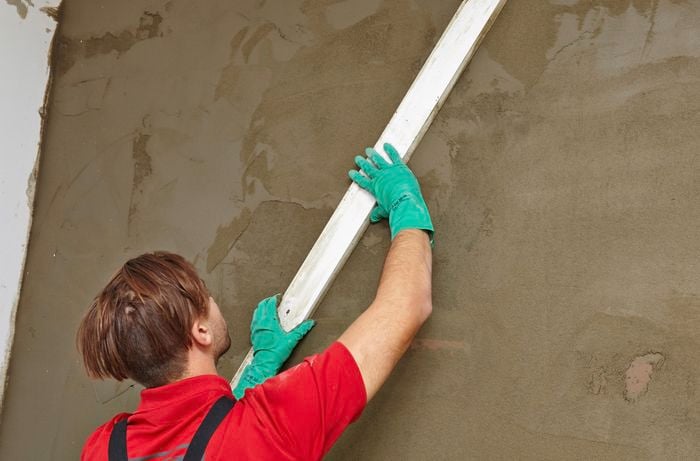 A person screeding a plastered wall with a straight edge