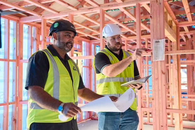 Two trade people with hard hats on walking on a building site