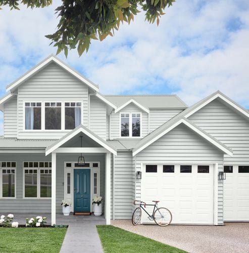 White weatherboard house with blue door, lawn front yard and a bicycle leaning against garage door