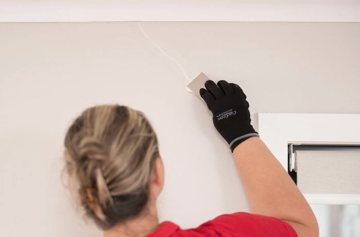 A person is using a putty knife to apply filler to a wall crack for repair. 