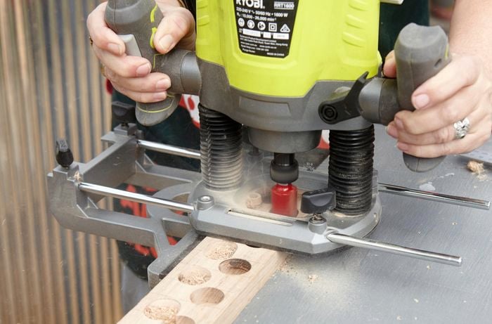 A person cutting round holes in timber using a router
