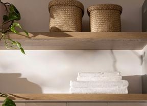 Open timber shelves with woven baskets, folded towels and trailing greenery.