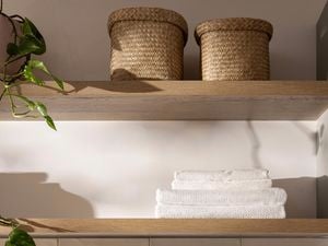 Open timber shelves with woven baskets, folded towels and trailing greenery.