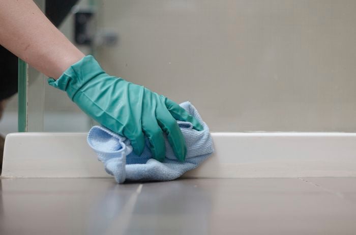 A hand wearing green gloves is wiping the surface with a microfibre cloth.