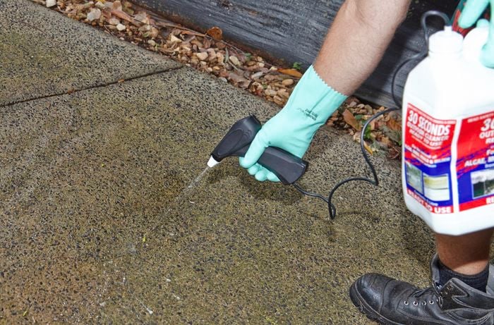 A person wearing protective gear spraying chemical cleaner on a driveway