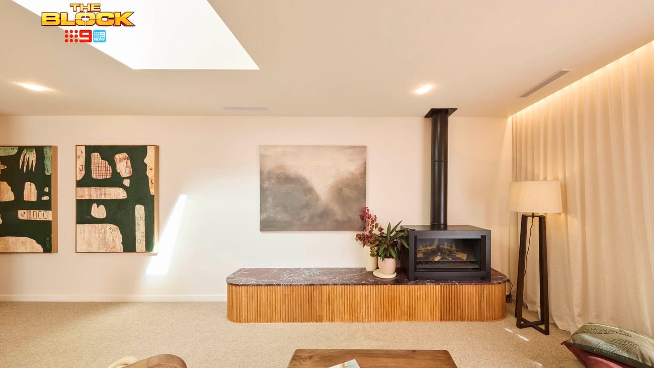 A modern living room with a skylight, featuring a fireplace, wall-mounted artwork, and a variety of contemporary furniture pieces.