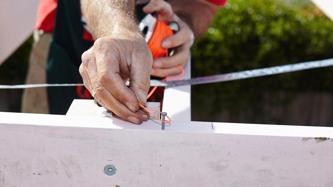 A person tying a loop of string around a nail in a bearer