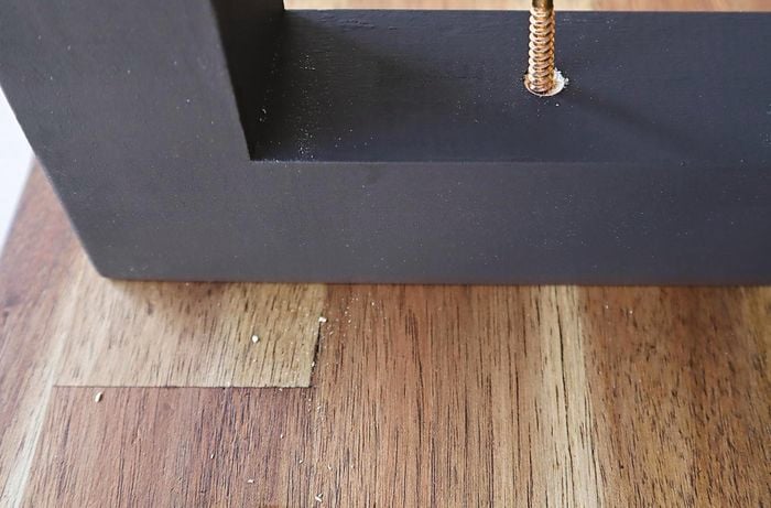 A screw being put into the underside of a desk frame