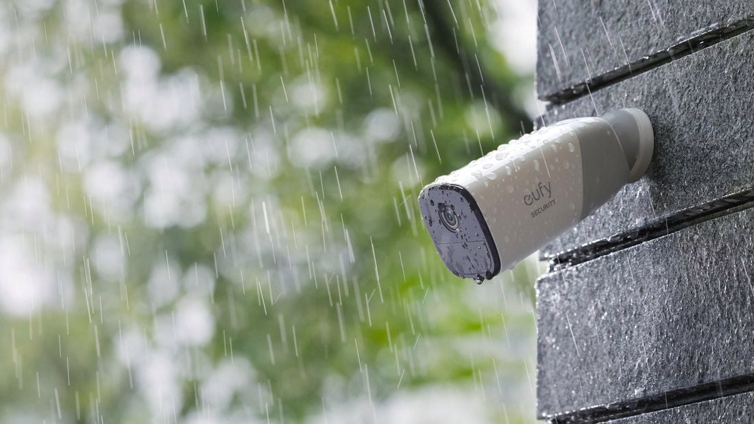 Close up of security camera on brick wall outside in rain.