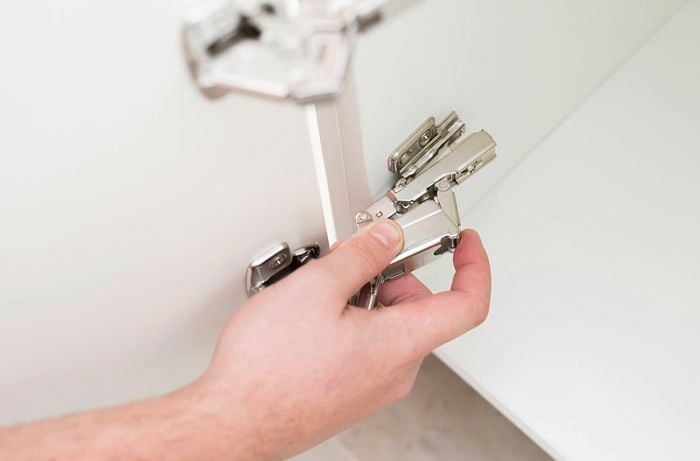 A person is attaching a cabinet door hinge to the mounting plate inside a cabinet.