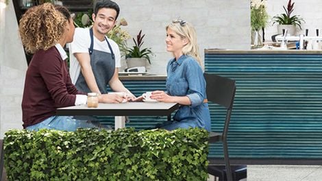 Two women sitting at an outdoor table being served by a waiter