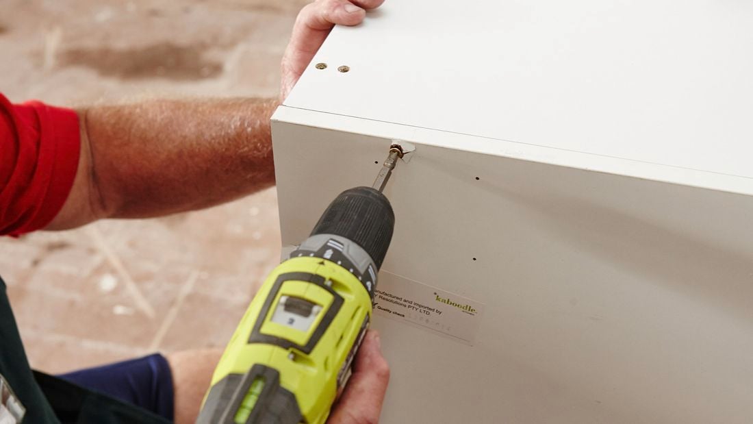 A person screwing a side panel to a cabinet using a cordless drill