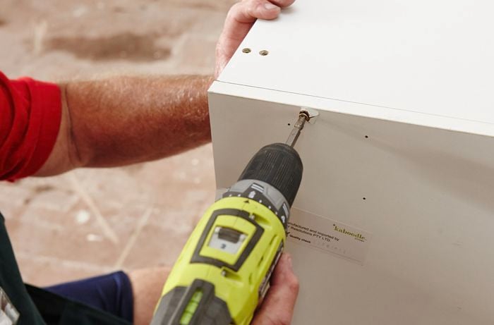 A person screwing a side panel to a cabinet using a cordless drill