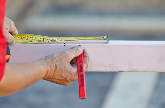 A wooden rail being marked with a pencil and tape measure