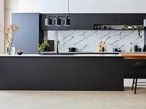 Modern kitchen featuring a matte black island bench, white marble-look splashback, black cabinetry and pendant lighting.