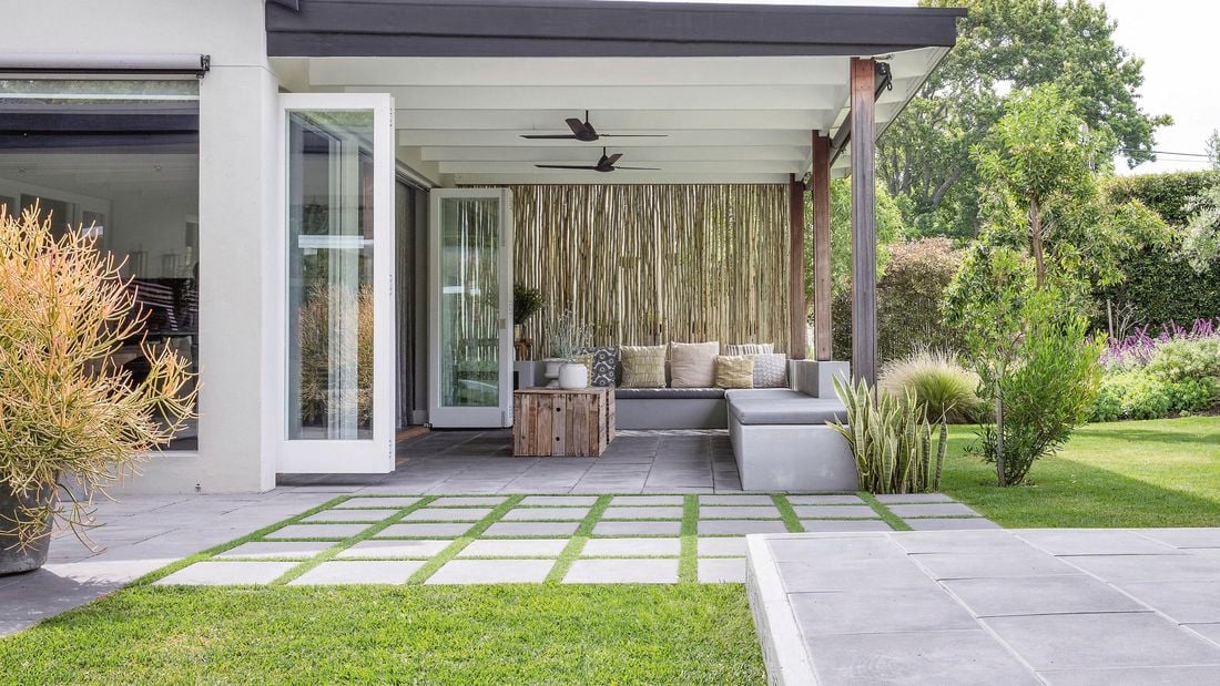 A patio space that opens from french doors, featuring geometric brick pavers on grass.