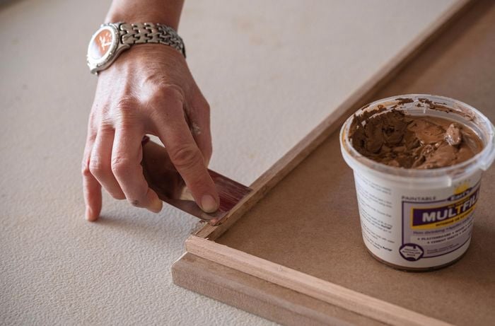 A person applying wood putty to fill the gaps.