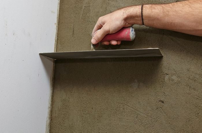 A person running a trowel down the corner of a plastered wall
