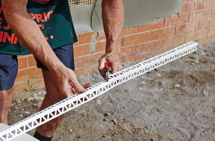 A person cutting a length of render trim bead using tin snips