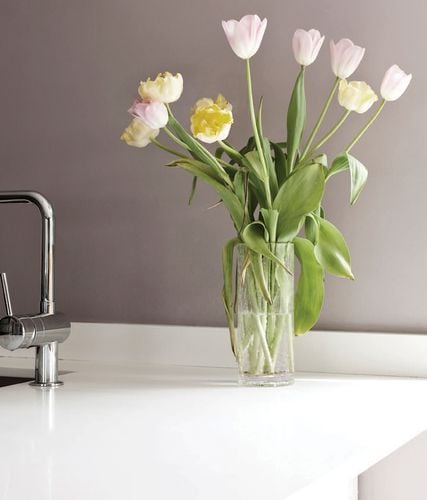 Close up of smooth white benchtop with mixer tap and vase of flowers