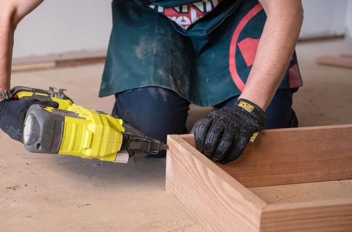 A person assembling the timber together to make the box using a nail gun.