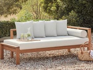 Outdoor timber setting with cushions on it outside on pebbles.