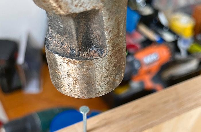 A person hammers a flathead nail into a moulding