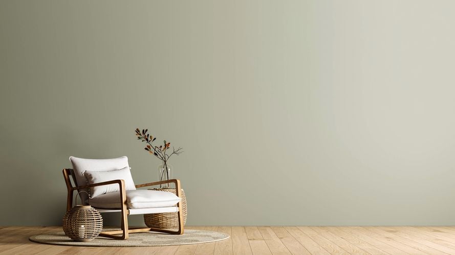 A room with a green wall, a chair and a plant in a basket in it.