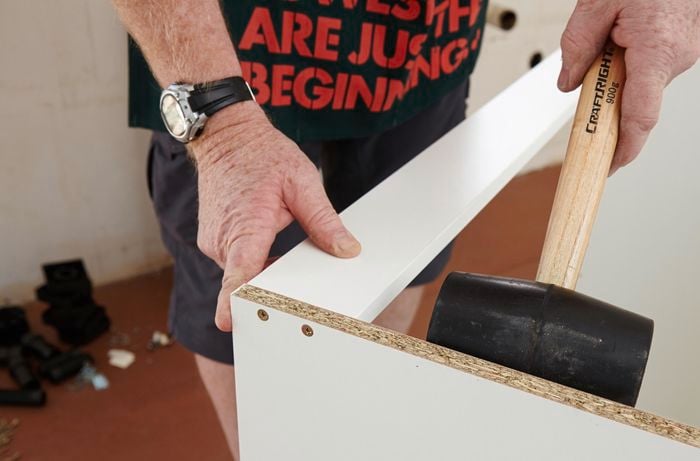 A person using a rubber mallet to position a rail in a cabinet