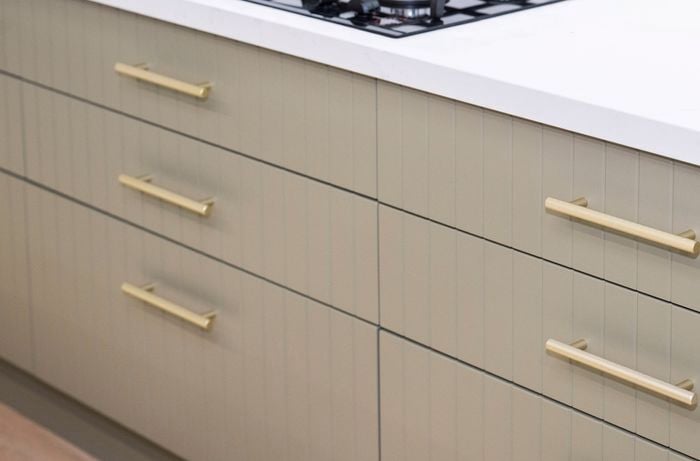 Beige drawers with gold handles, underneath a white bench top in a kitchen.