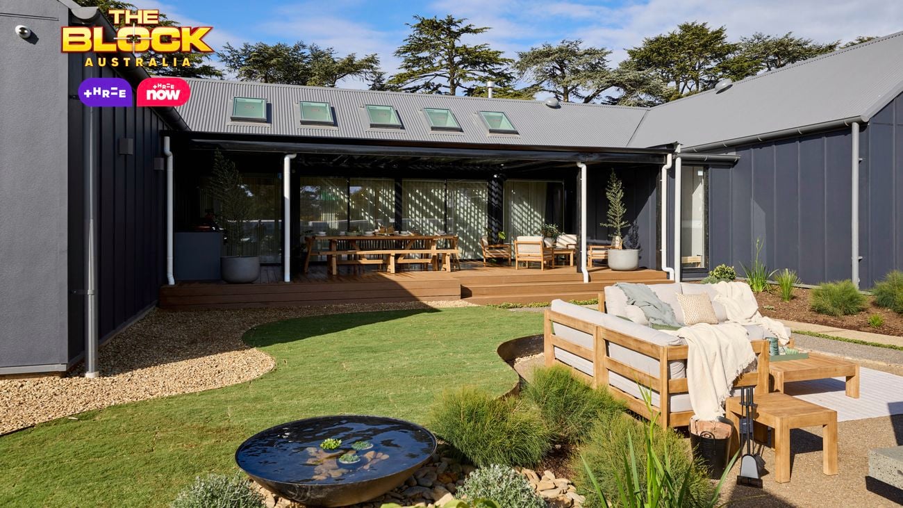 The back of a house with an outdoor setting on the grass area, a rocks area and an outdoor setting and table and chairs on decking.