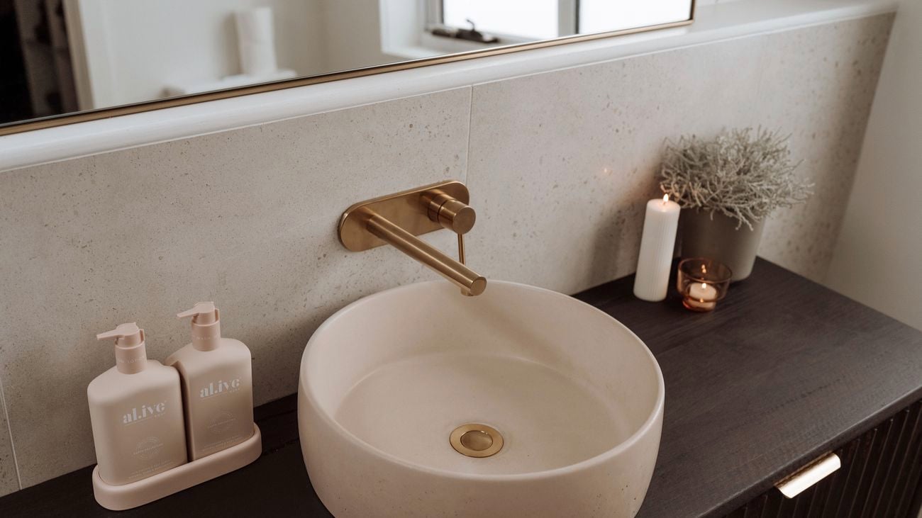 Dark brown wood cabinet with a round pink sink with a gold tap and two pink bottles on the side.